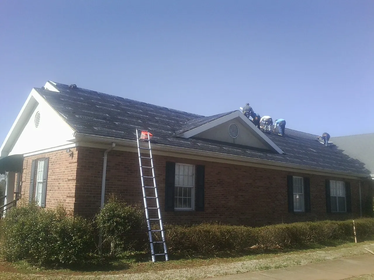 Crew tearing shingles off a brick ranch roof with a ladder set — Metal Roof Repair work by our crew in Roachdale