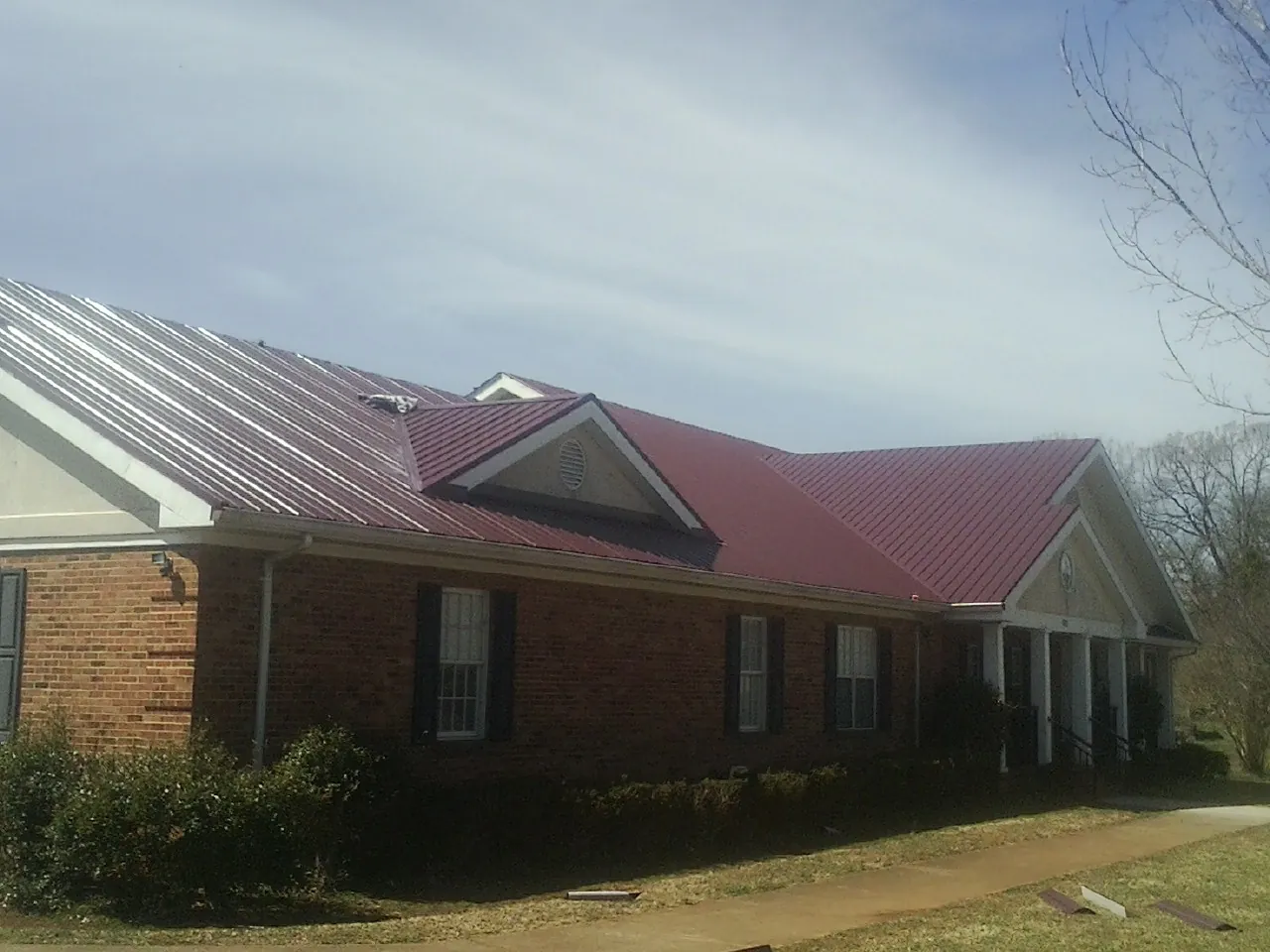 Red metal roof with gabled entries on a long brick building, from a Hail Damage Roof Repair job in Roachdale