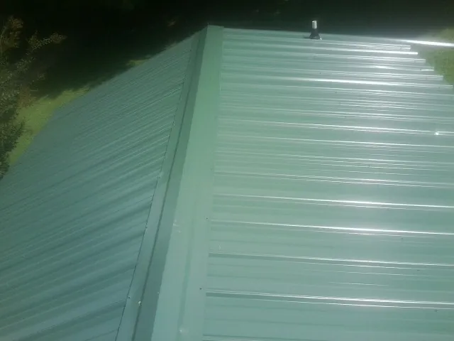 New green metal panels meeting at the ridge of a roof — Flat Roof Repair work by our crew in Roachdale