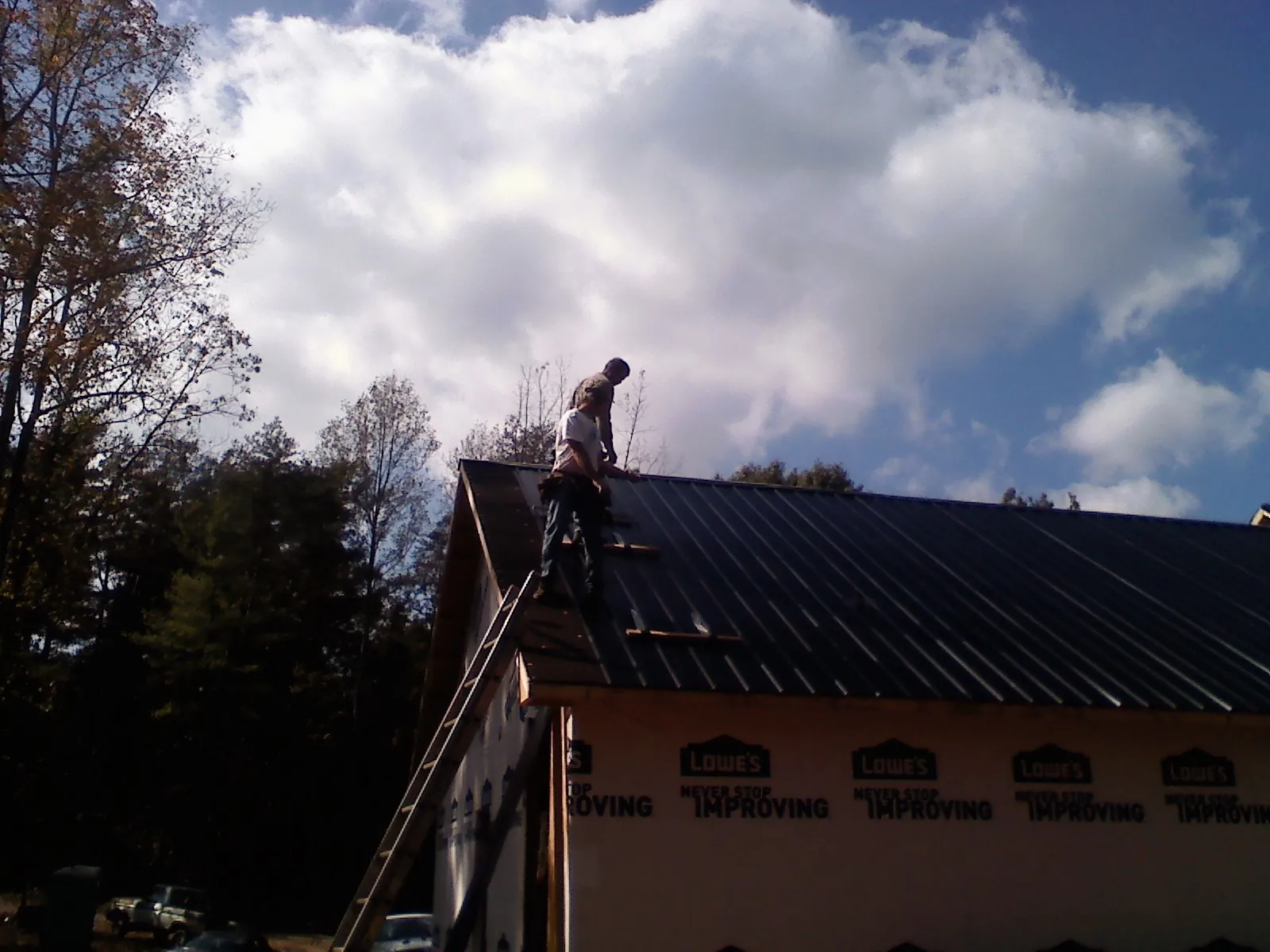 Roofer fastening dark metal panels high against a cloudy sky, from a Roof Inspection job in Roachdale
