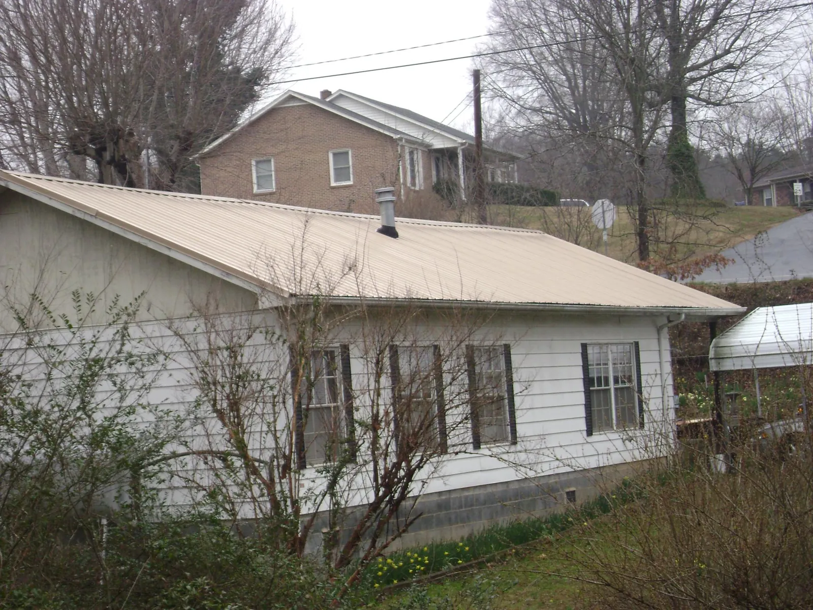Tan metal roof on a white sided house set into a hillside — Commercial Roofing by Roofing Brothers in Roachdale