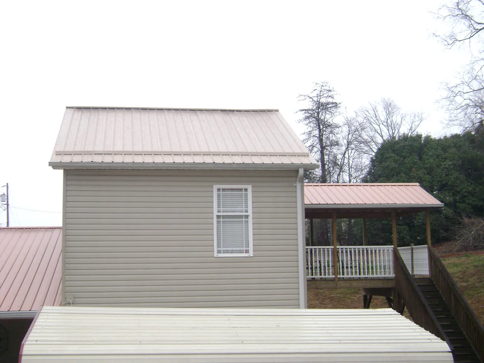 Tan metal roofs on a two story addition and attached porch, from a Roof Replacement job in Roachdale